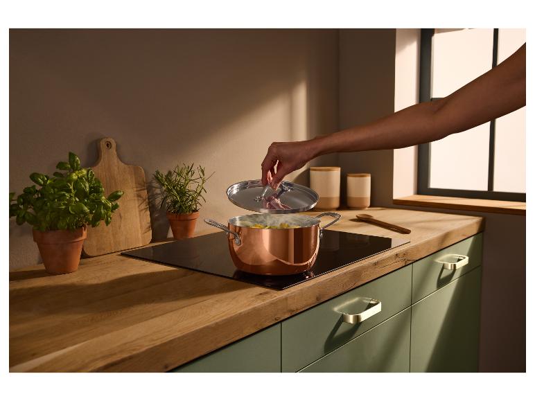 Keuken met houten aanrechtblad, groene kasten en een koperen pan op de kookplaat.