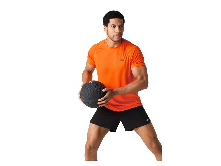 Een man in een oranje shirt en zwarte shorts houdt een medicijnbal vast.