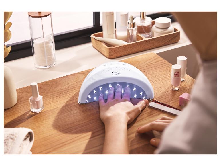 Vrouw droogt nagels in een UV-lamp, met nagellakken en manicurebenodigdheden.