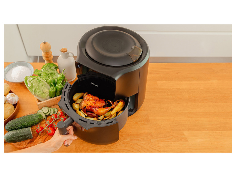 Een zwarte airfryer van Cecotec met een gebakken kip en frietjes.