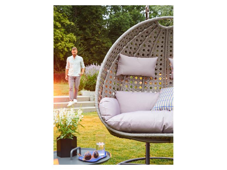 Hangstoel met kussens en een man die een trap afloopt in een tuin.