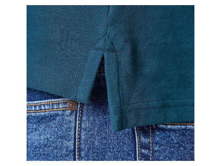 Detail van een petrolkleurig piqué shirt met zijsplitten over een blauwe jeans.