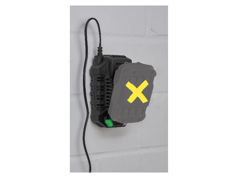 Zwarte acculader met een grijze accu met een gele X, gemonteerd aan een bakstenen muur.
