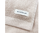 Close-up van een beige handdoek met een wit label met een logo en tekst.