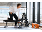 Man doet dumbbell rows op een halterbank, met een halterrek in de buurt.