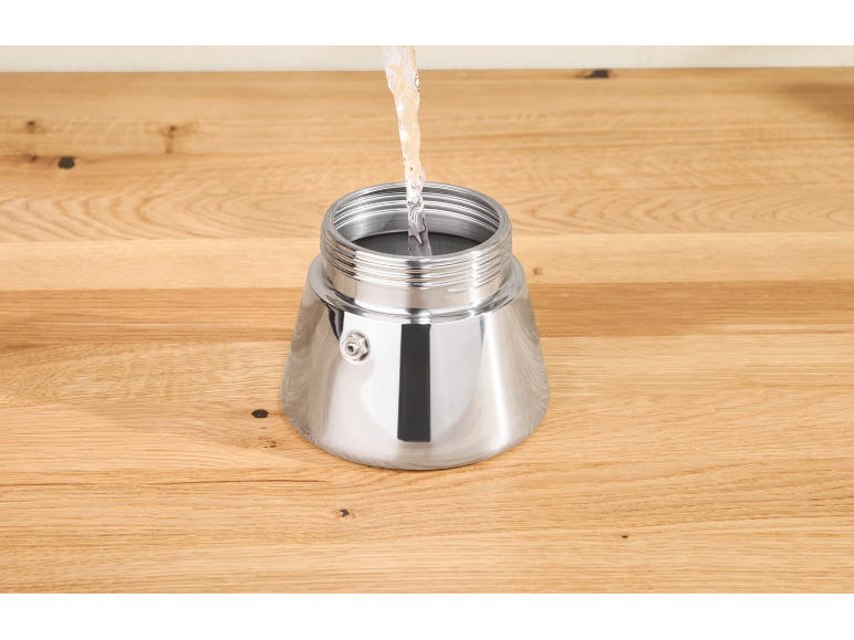 Water wordt in de zilveren basis van een koffiezetapparaat op een houten tafel gegoten.