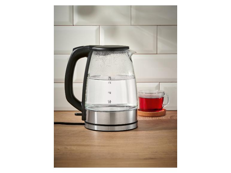 Glazen waterkoker met water en een kop rode thee op een houten tafel.