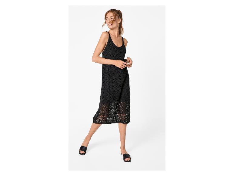 Vrouw in een zwarte gehaakte spaghettibandjesjurk en zwarte sandalen.