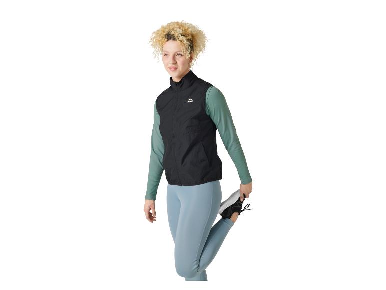 Vrouw met krullend haar die zich uitrekt, draagt een Crivit sportvest en blauwe leggings.