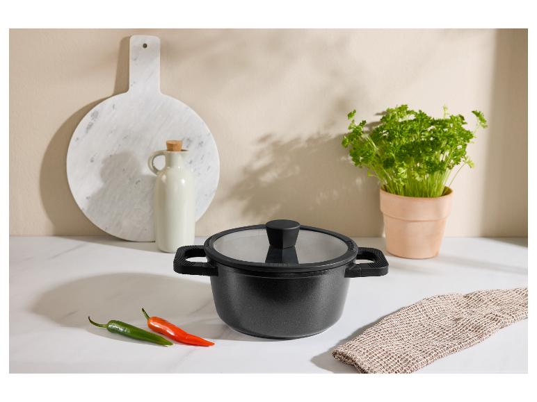 Zwarte pan met deksel, pepers, snijplank en kruiden in een keukenomgeving