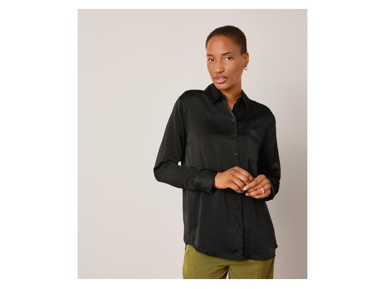 Een model draagt een zwarte satijnen blouse met lange mouwen.