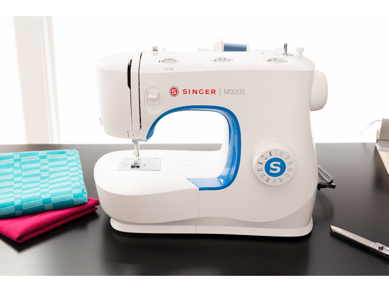 Witte naaimachine met blauwe accenten, stof en schaar op een donkere tafel.