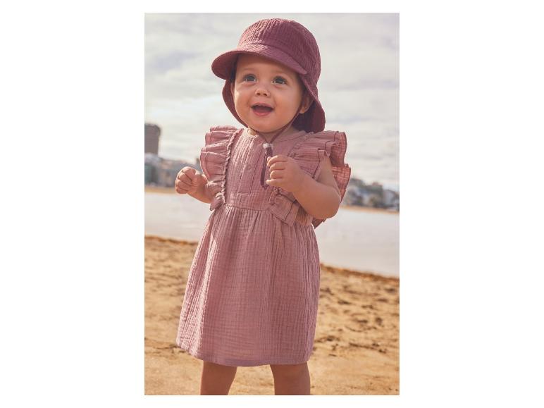 Baby in roze jurk en zonnehoed op het strand