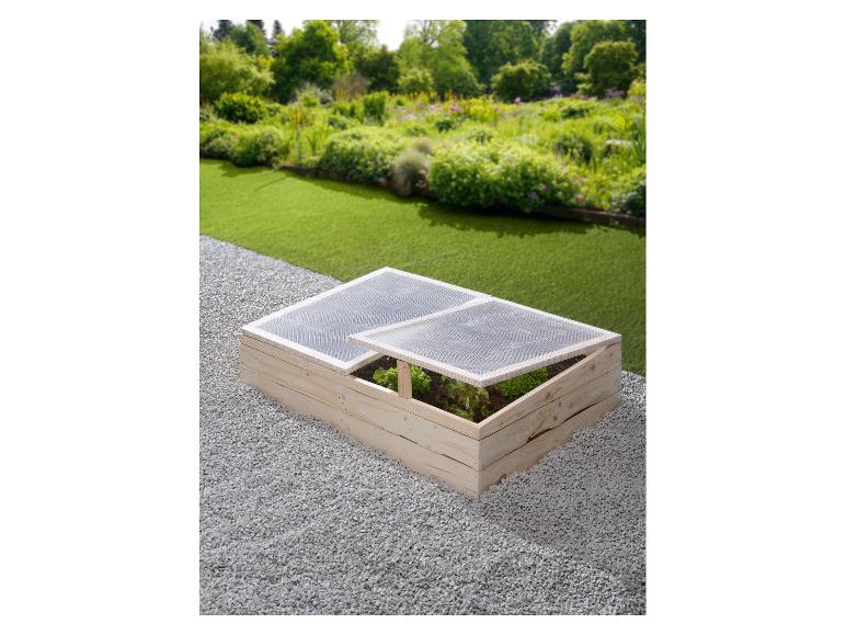 Houten koude bak met transparant deksel en groenten in de tuin.