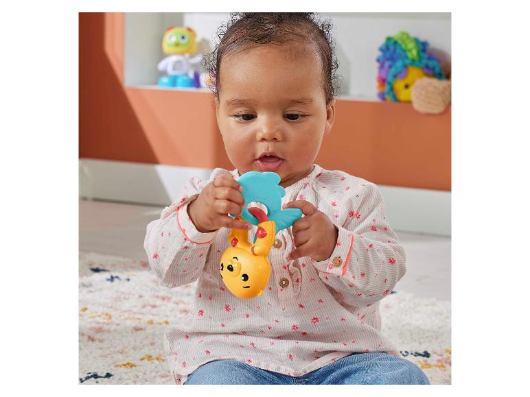 Een zittende baby speelt met een gele en blauwe speelgoedrammelaar.