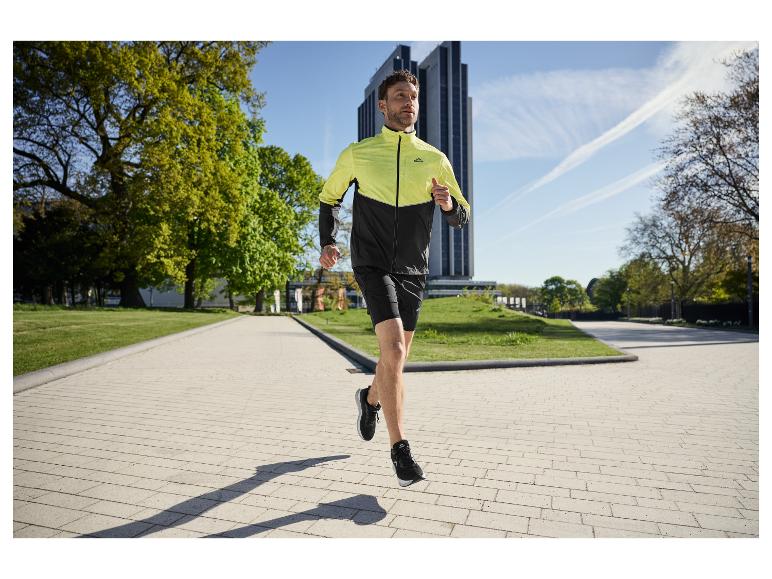 Man rent in een park, draagt een tweekleurig hardloopjack en zwarte shorts.