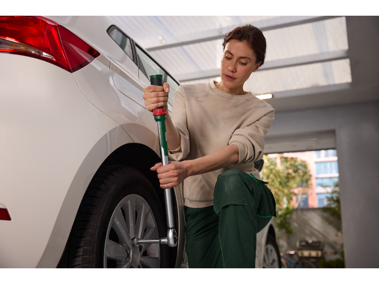 Vrouw verwisselt een autoband met een kruissleutel in een garage.