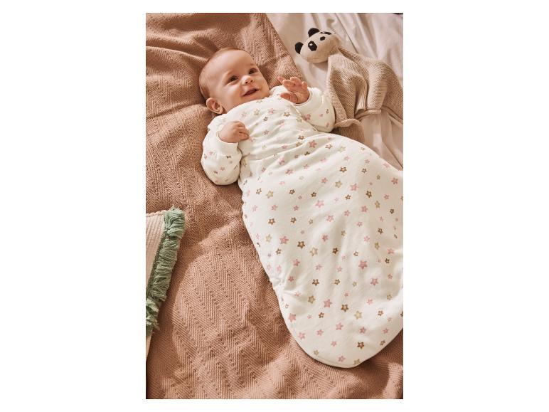 Baby in sterren slaapzak, liggend op deken met panda knuffel.