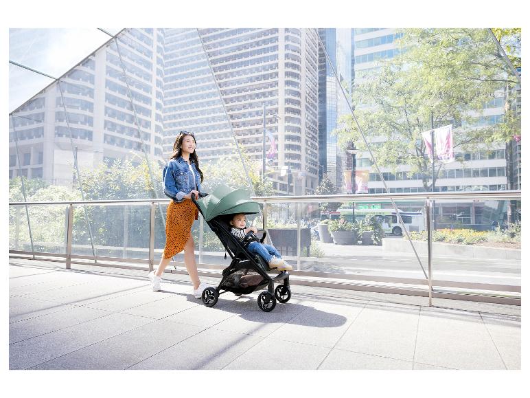 Vrouw duwt kinderwagen met baby in stedelijke omgeving.