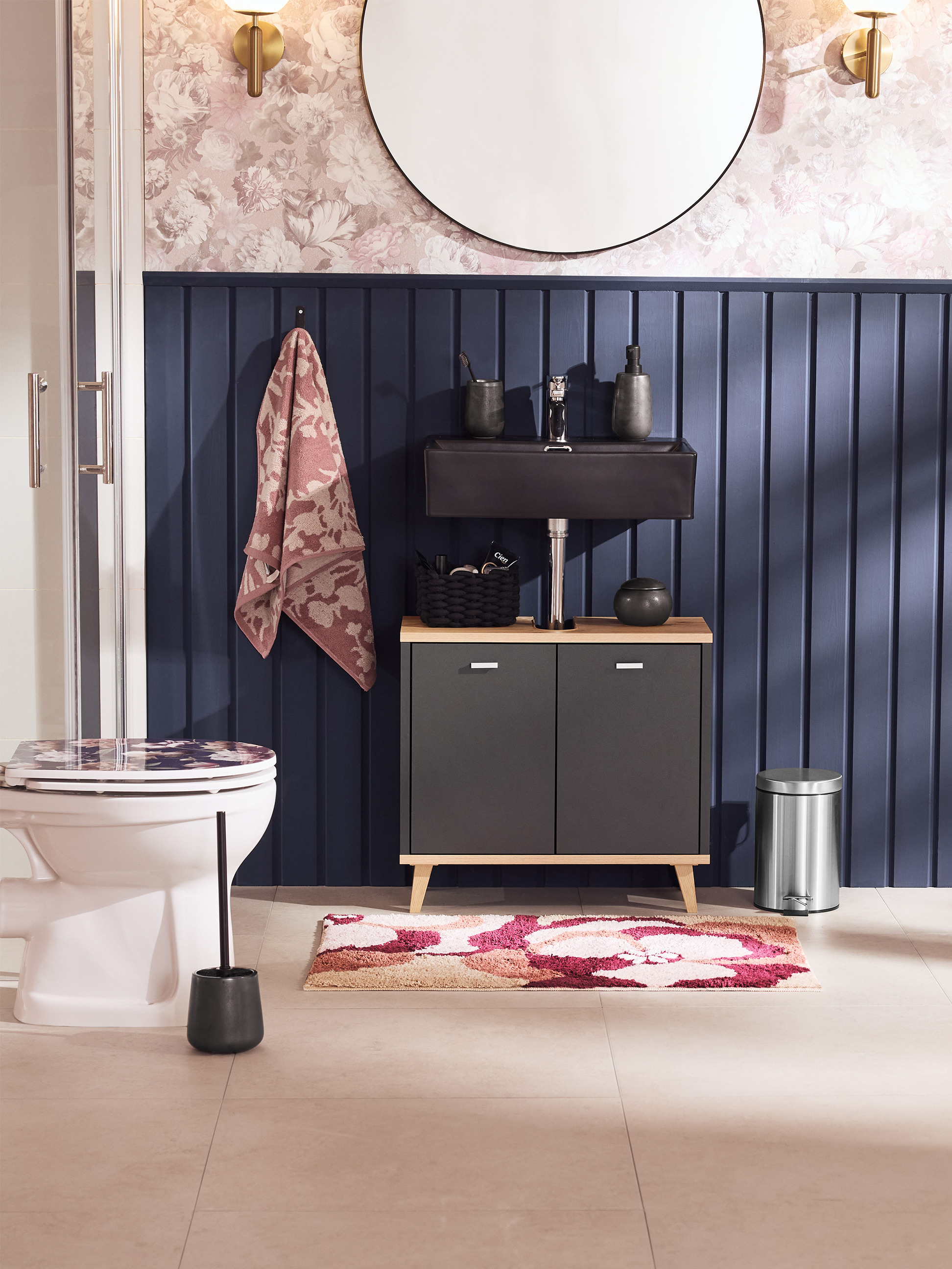 Badkamer met toilet, wastafel, kast en bloemig vloerkleed.