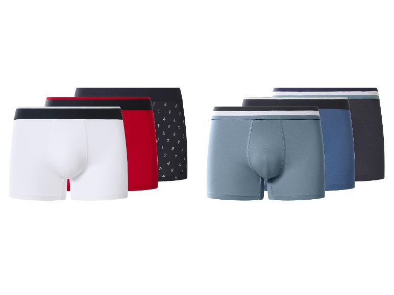 Zes herenboxershorts in diverse kleuren en patronen, waaronder effen en met ankerprint.