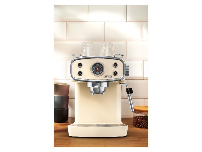 Crèmekleurig retro koffiezetapparaat met manometer, op houten aanrecht met kopjes en koffiebonen.