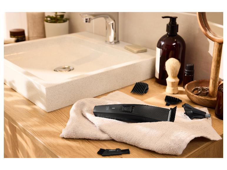 Haartrimmer en accessoires op een handdoek in een badkamer met wastafel.