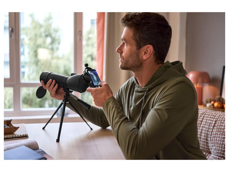 Een man gebruikt een zwarte telescoop met een smartphone op een statief.