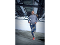 Vrouw in sporttrui en legging rent onder een metalen constructie.