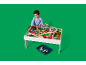 Een klein kind speelt met een houten treinset op een witte tafel.