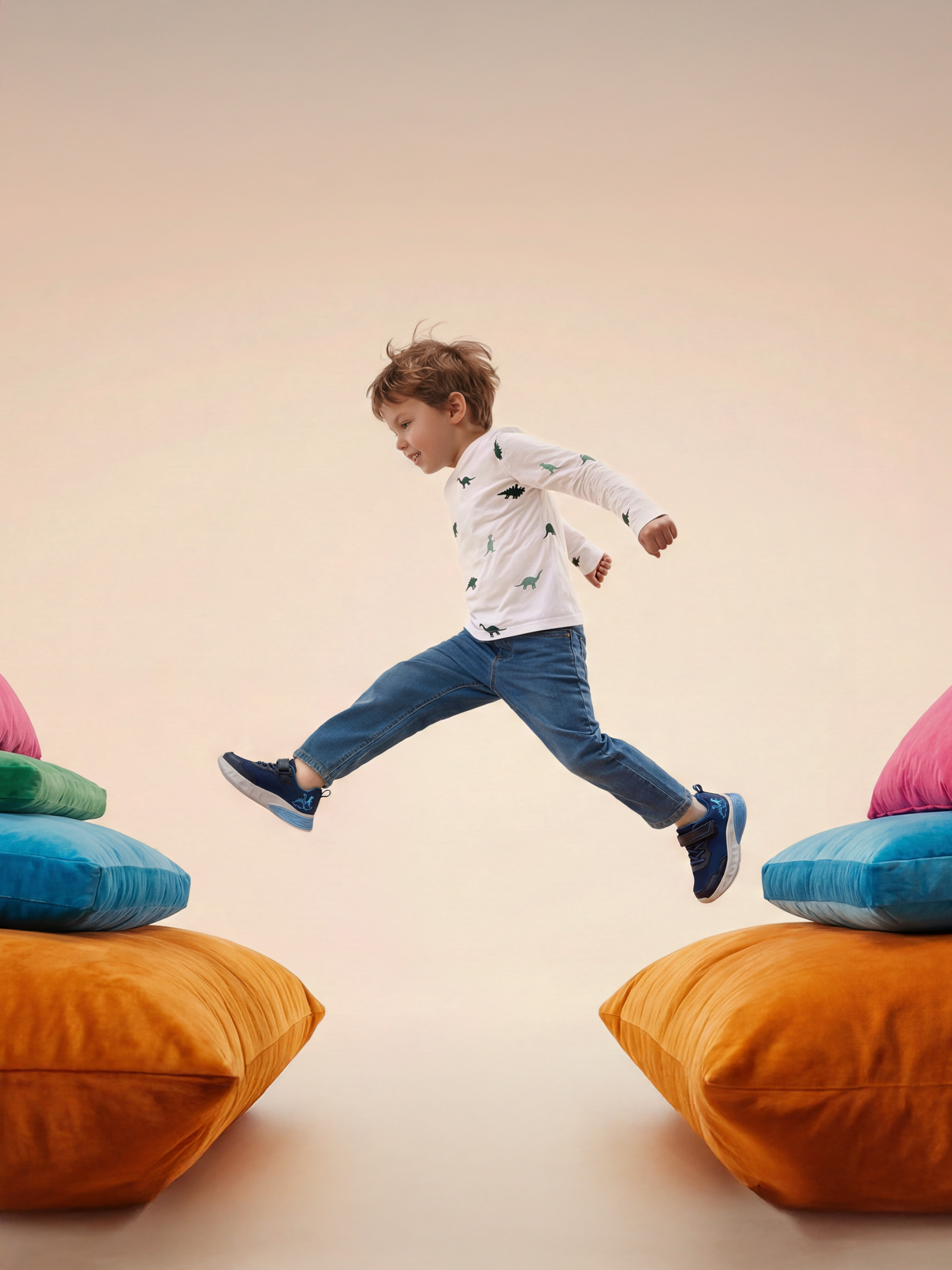 Kind springt tussen kleurrijke kussens, draagt een dinosaurus T-shirt en jeans.