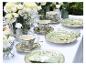 Tafel gedekt met groen servies met vogelthema en witte bloemen, met gouden vorken.