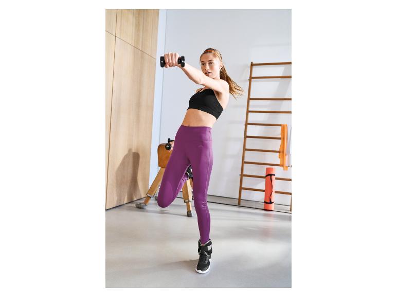 Vrouw in zwarte sportbeha en paarse legging oefent met dumbbells
