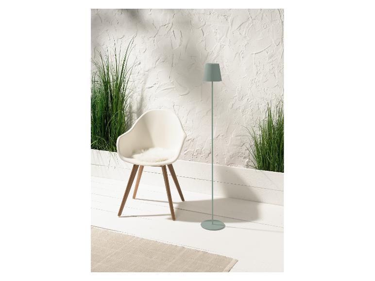 Designstoel, staande lamp en groene planten in een minimalistische setting.