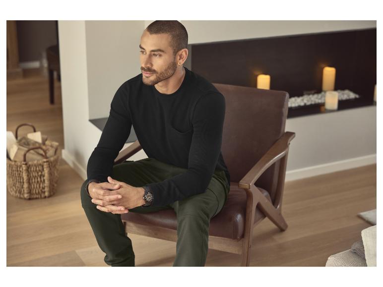 Man in zwart shirt met lange mouwen en groene broek zit in een leren stoel.