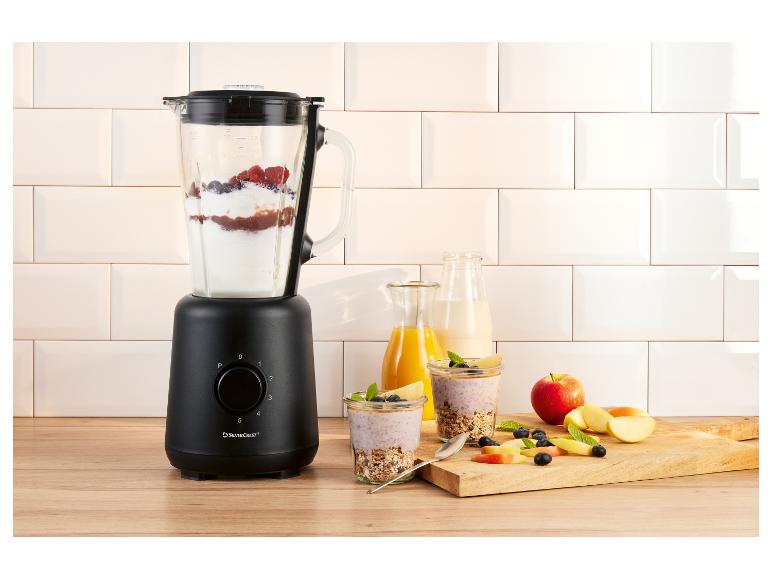 Zwarte blender met bessen en yoghurt, naast glazen met ontbijt en fruit.