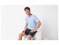 Man in blauw T-shirt en donkere shorts zit en lacht.