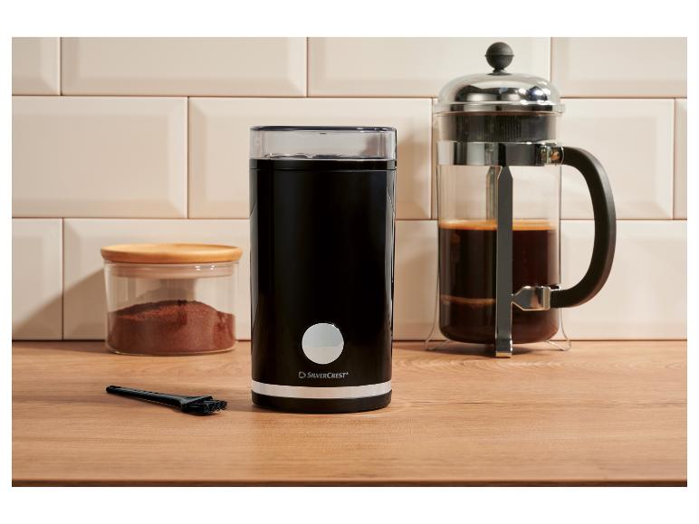 Zwarte elektrische koffiemolen, cafetière en pot gemalen koffie op een houten aanrecht.