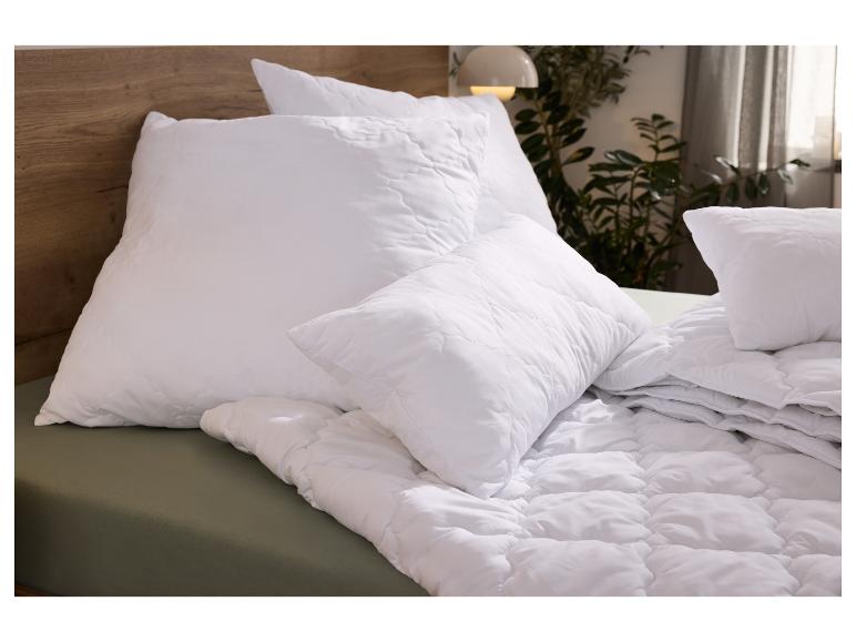 Wit gewatteerd kussen en dekbed op een bed met houten hoofdbord en groen laken.