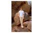 Man in lichtblauw T-shirt en beige broek staat tussen rotsformaties.