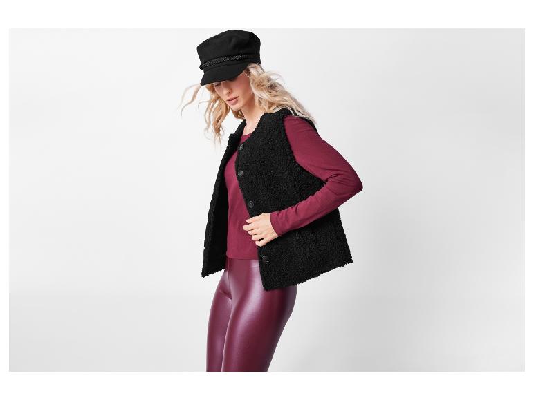 Een vrouw draagt een zwart schapenvacht vest en bordeauxrode leggings.