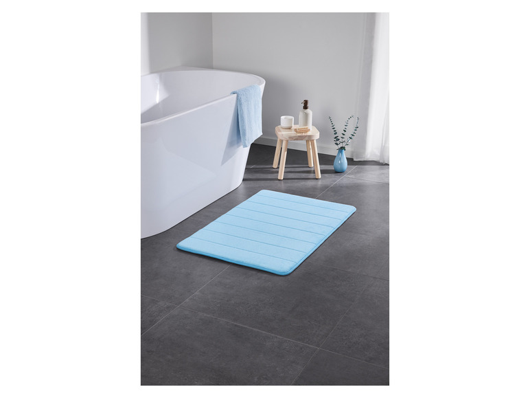 Een lichtblauwe badmat in een badkamer met een badkuip.