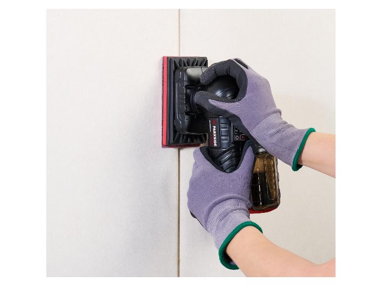 Een persoon schuurt een muur met een elektrische schuurmachine, met beschermende handschoenen.