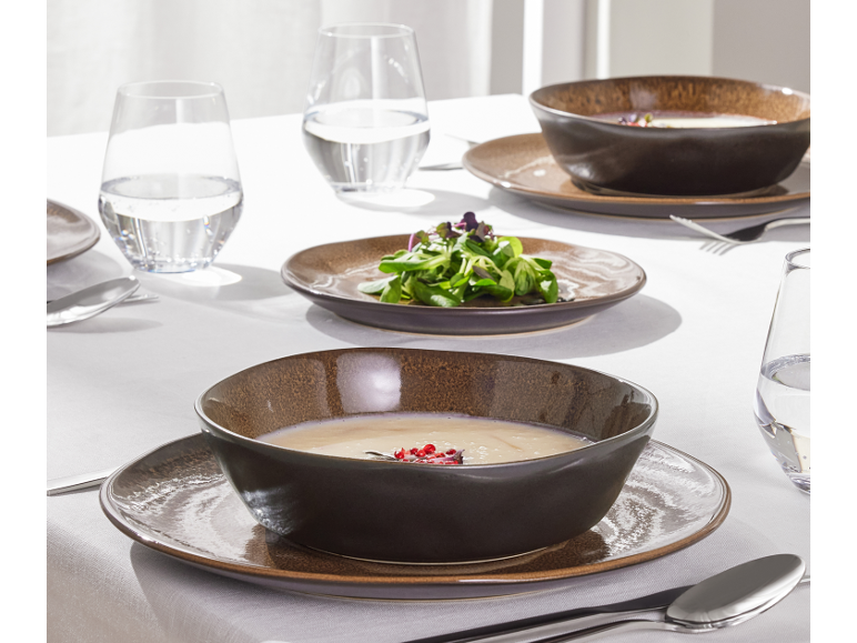 Tafel gedekt met donkerbruine keramische kommen en borden, glazen water en bestek.