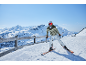 Skiër in een groene ski-jas en witte skibroek op een besneeuwde berghelling.