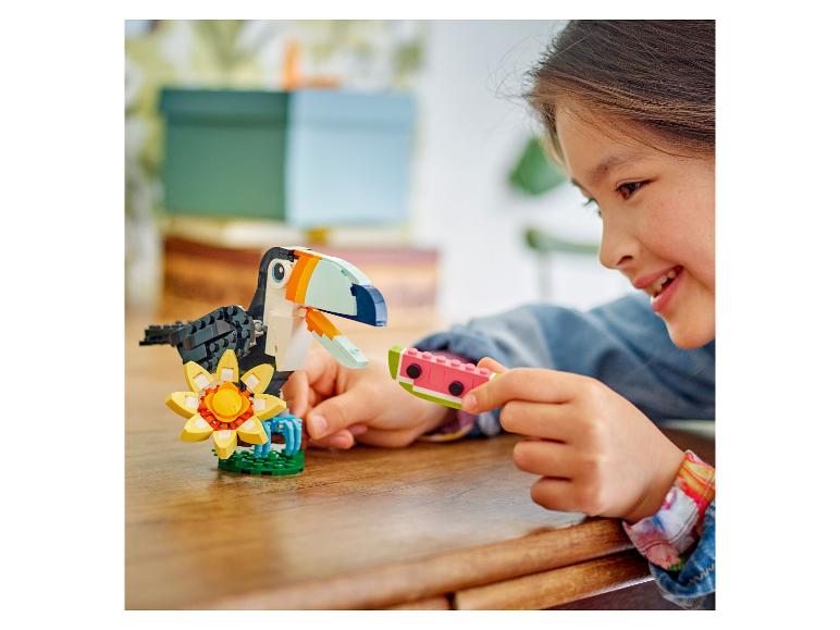 Een meisje lacht terwijl ze een LEGO watermeloenstuk vasthoudt bij een LEGO toekan en bloem.