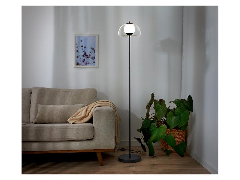 Moderne staande lamp met glazen kap, naast een bank.