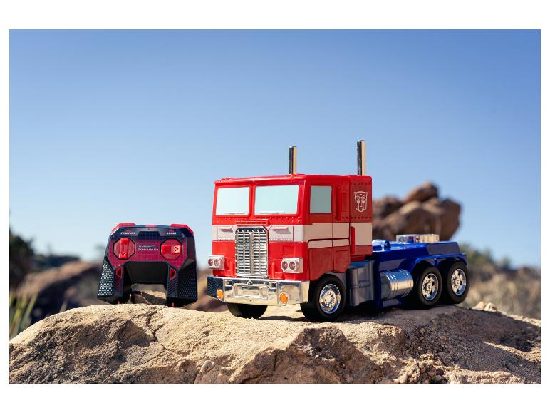 Een Optimus Prime speelgoedtruck en een afstandsbediening op rotsachtig terrein onder een heldere hemel.