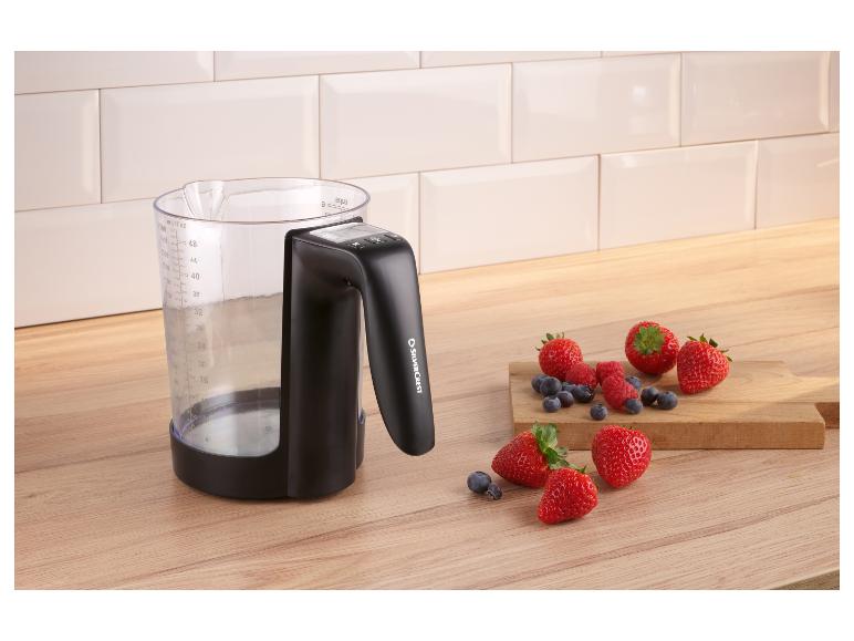 Maatbeker met handvat en bessen op een houten aanrecht.