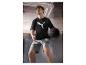 Man in zwart T-shirt en grijze korte broek houdt een medicijnbal vast in een sportschool.